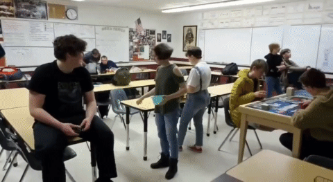 GIF panning around room, showing students eating & playing games.